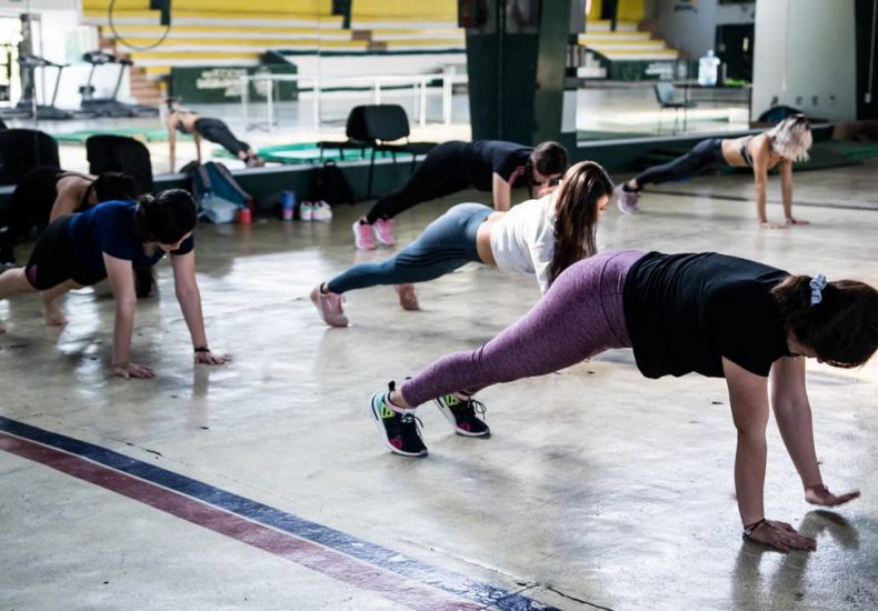 Group of women doing push-ups in a gym reflecting in a mirror.